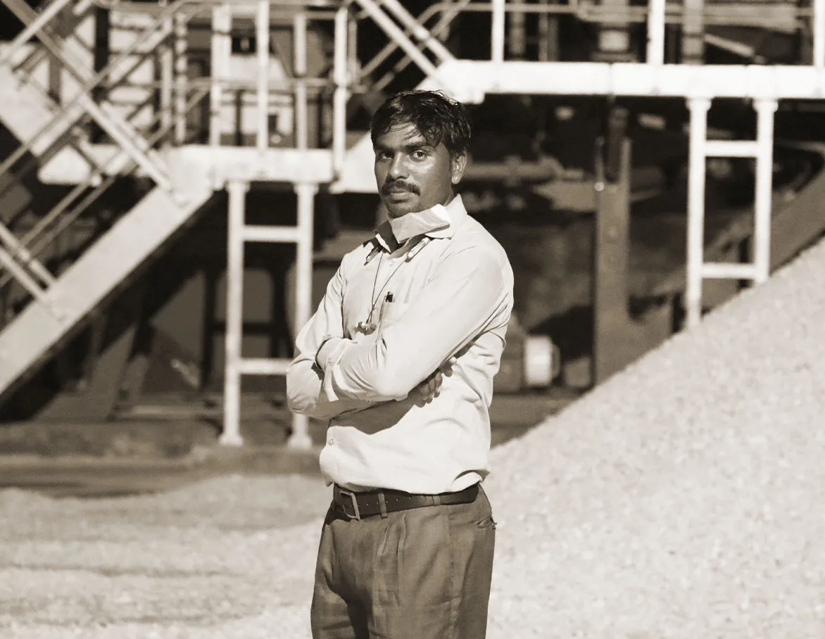 A plant operator standing with folded arms in front of the washing plant steelwork and a stockpile