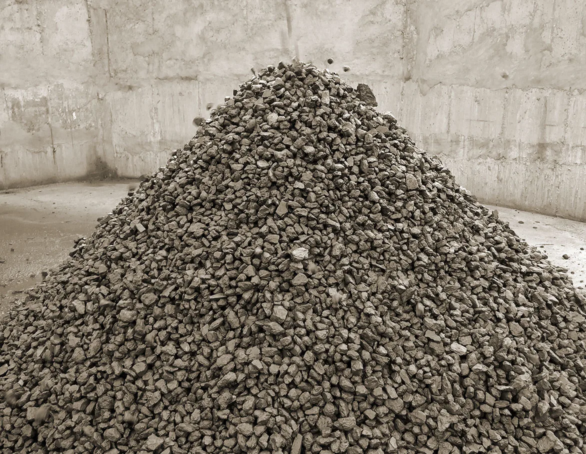 A conical stockpile of crushed aggregate inside a walled bay at a quarry