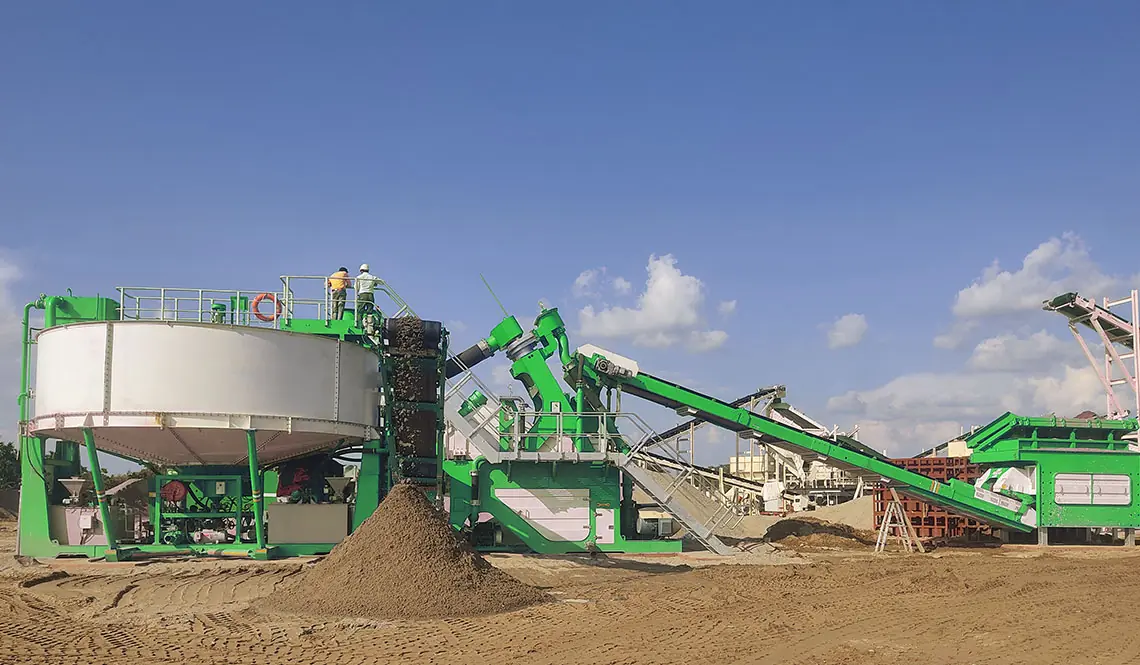 A green CFlo plant with a circular thickener under a blue sky, discharging graded sand stockpiles