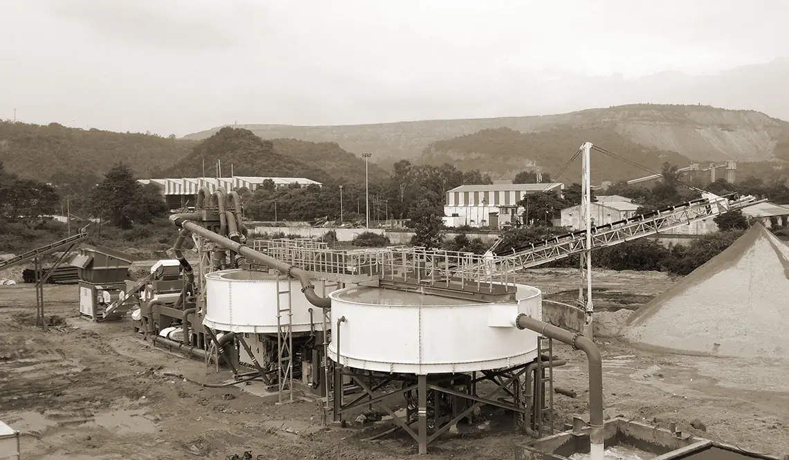 A washing plant with two circular tanks in a valley, buildings and hills behind