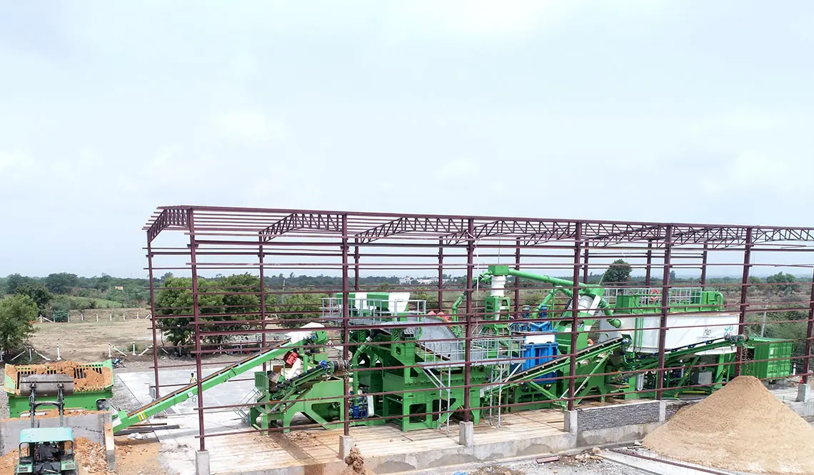 A green CFlo plant being erected inside a new steel-framed building, sand stockpiles alongside